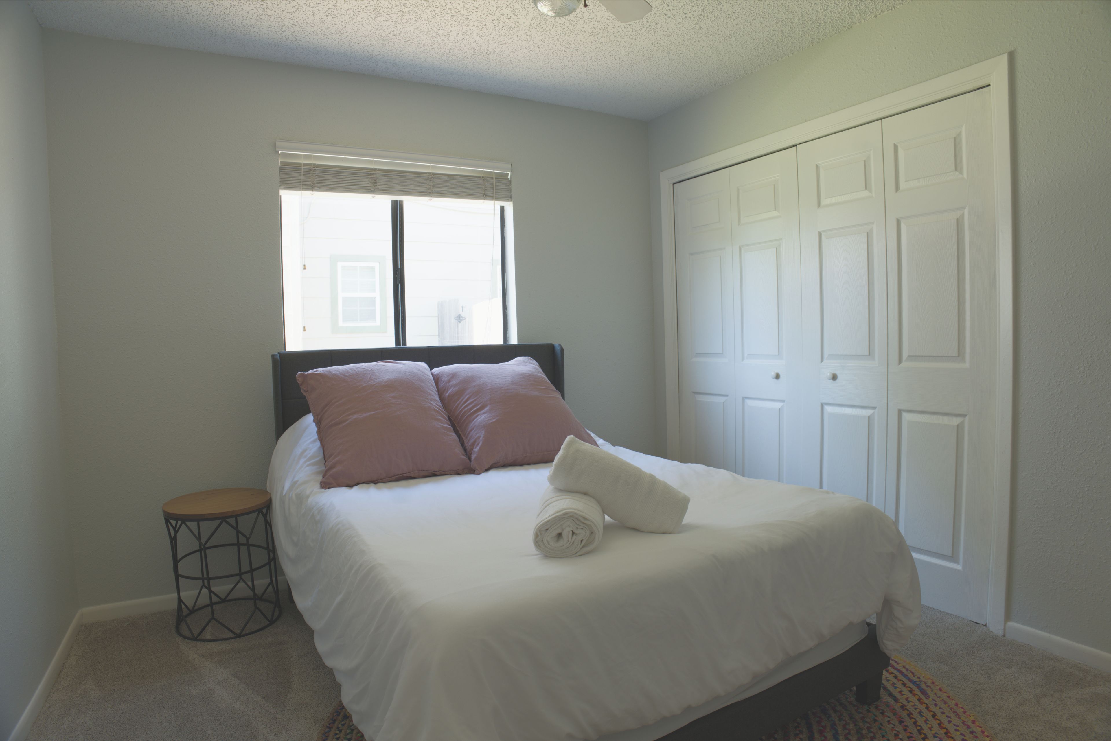 A bedroom with a bed, a window, a door, and a small round table.