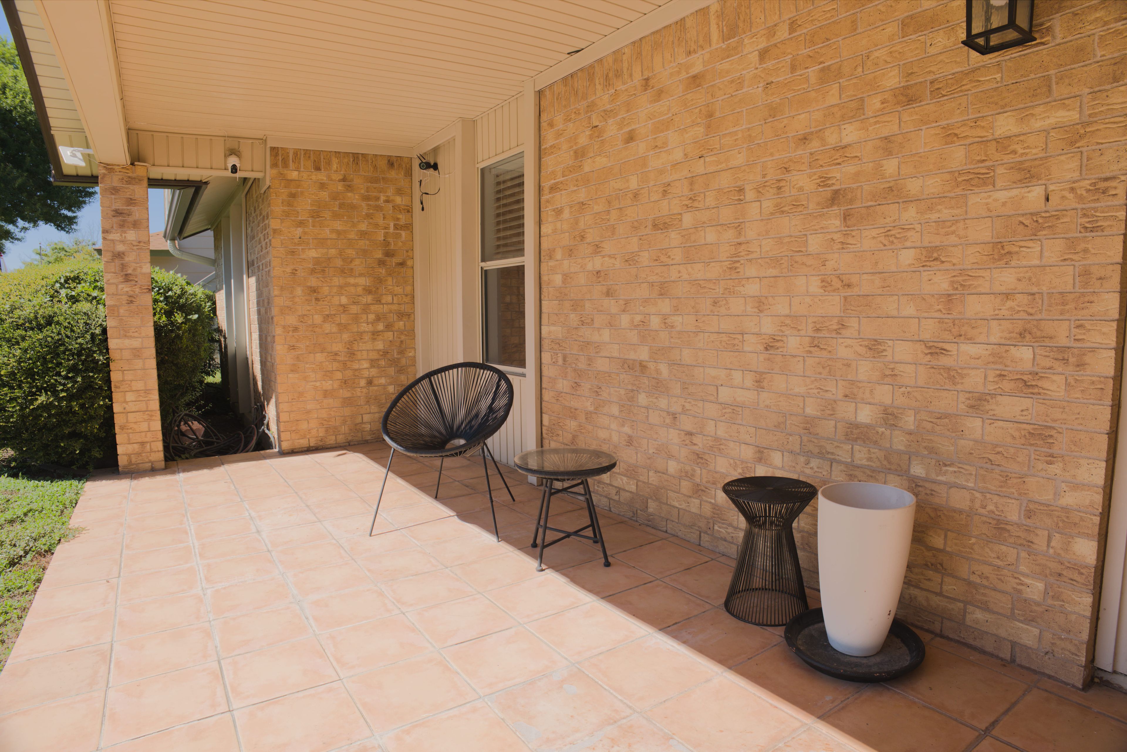 A covered patio area with a brick wall, a chair, a small table, and a potted plant.
