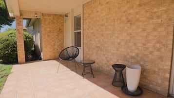 A covered patio area with a brick wall, a chair, a small table, and a potted plant.