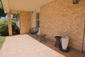 A covered patio area with a brick wall, a chair, a small table, and a potted plant.