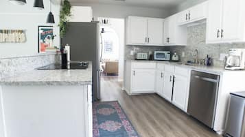 Une cuisine moderne avec des meubles blancs, un plan de travail en granit, des appareils électroménagers en acier inoxydable et un tapis à motifs.