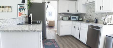 A modern kitchen with white cabinets, a granite countertop, stainless steel appliances, and a patterned rug.