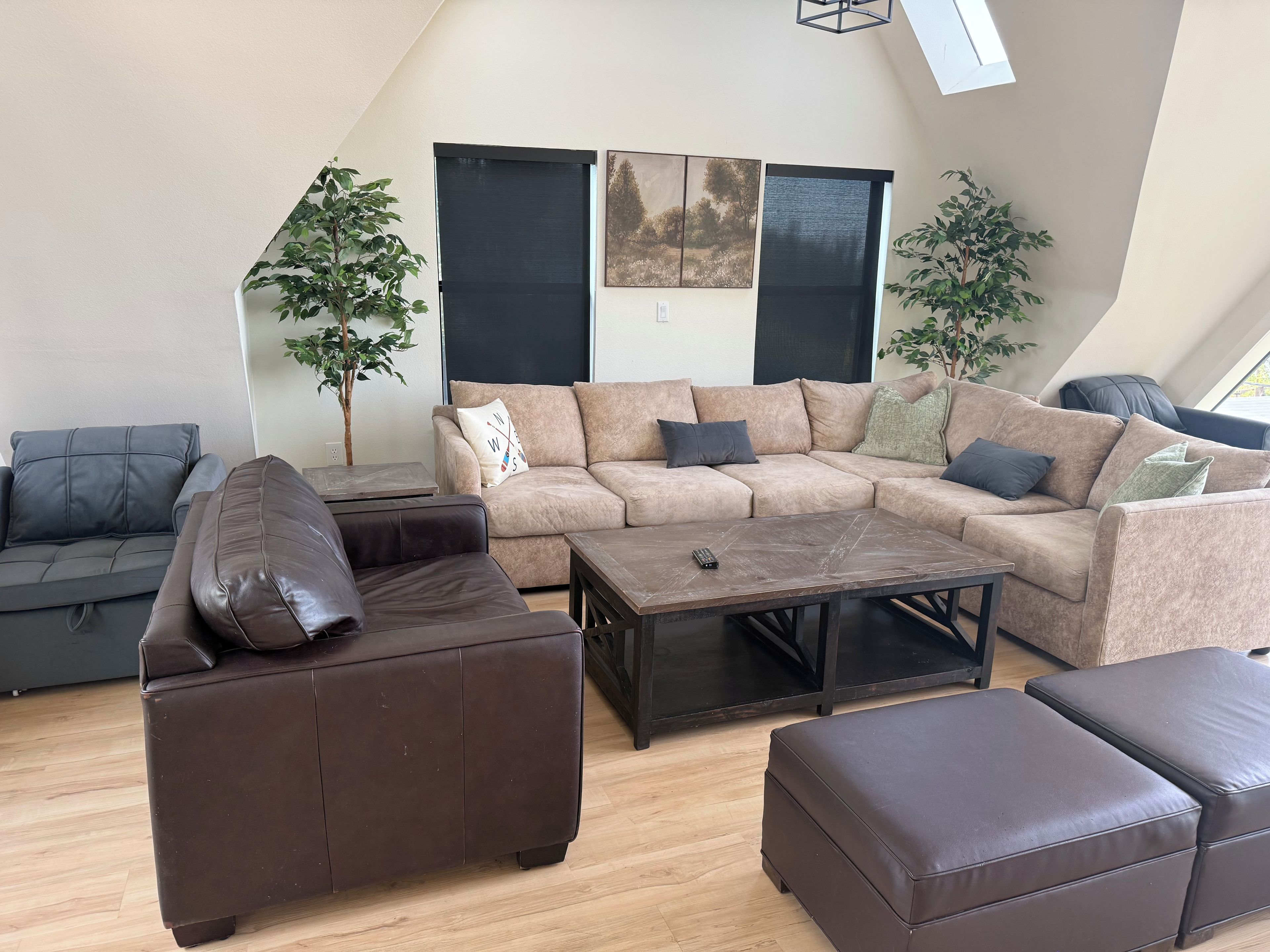 Ein modernes Wohnzimmer mit einem Ecksofa, einem braunen Ledersitzhocker und einem Couchtisch.