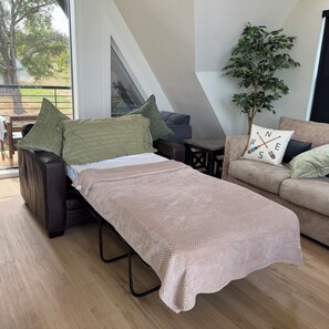 A modern living room with a bed, a sofa, a coffee table, and a potted plant.