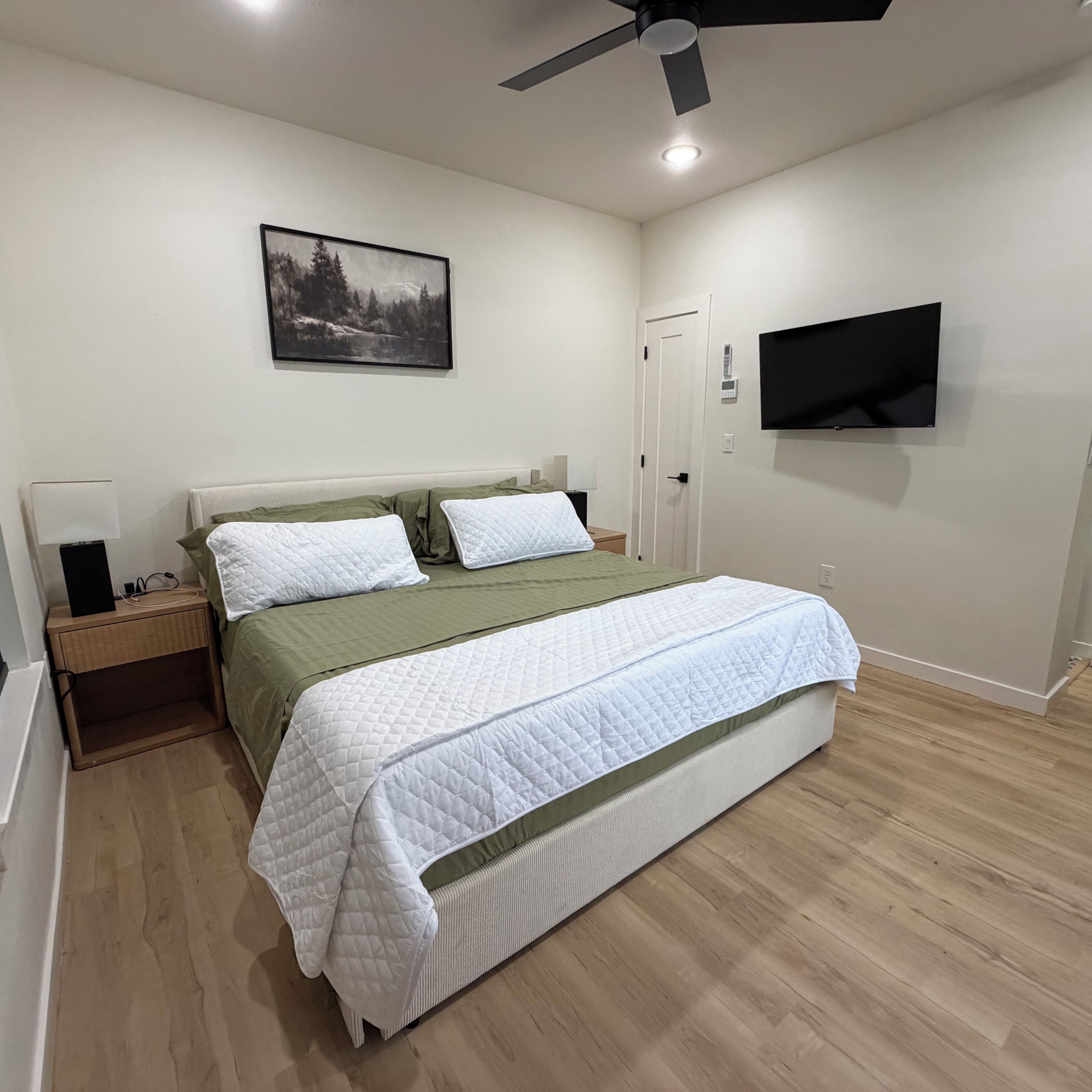 Ein Schlafzimmer mit einem Bett, einem Nachttisch, einem an der Wand befestigten Fernseher und einem Deckenventilator.