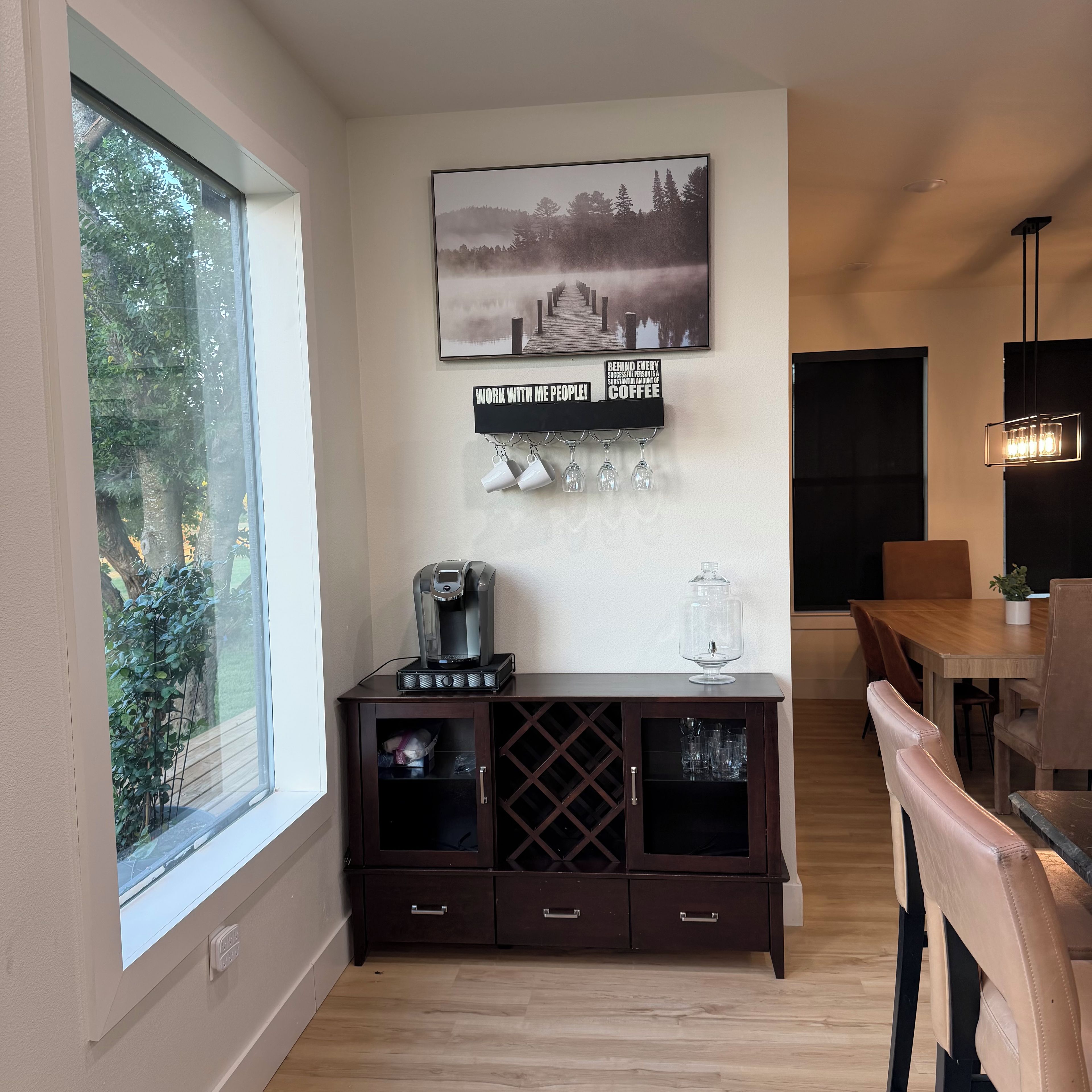 A modern kitchen with a coffee machine, a wine cooler, and a dining area with wooden furniture.