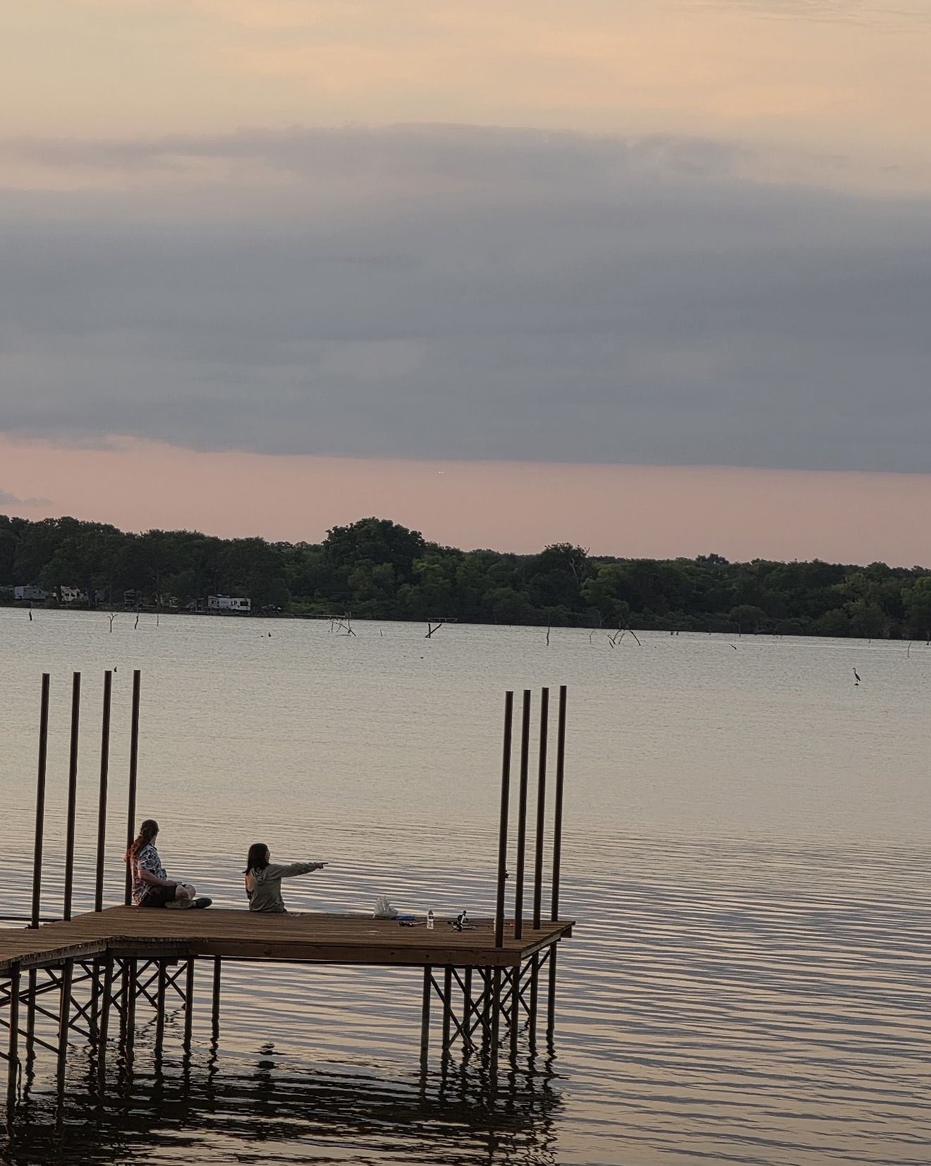A wooden dock extending into calm water with two individuals seated at the end.