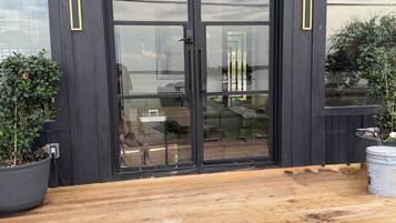 A wooden deck with a black-framed glass door leading to an outdoor seating area.