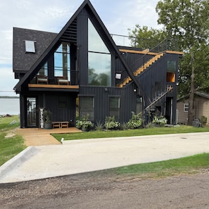 A modern two-story house with a large glass window, a wooden deck, and a staircase.
