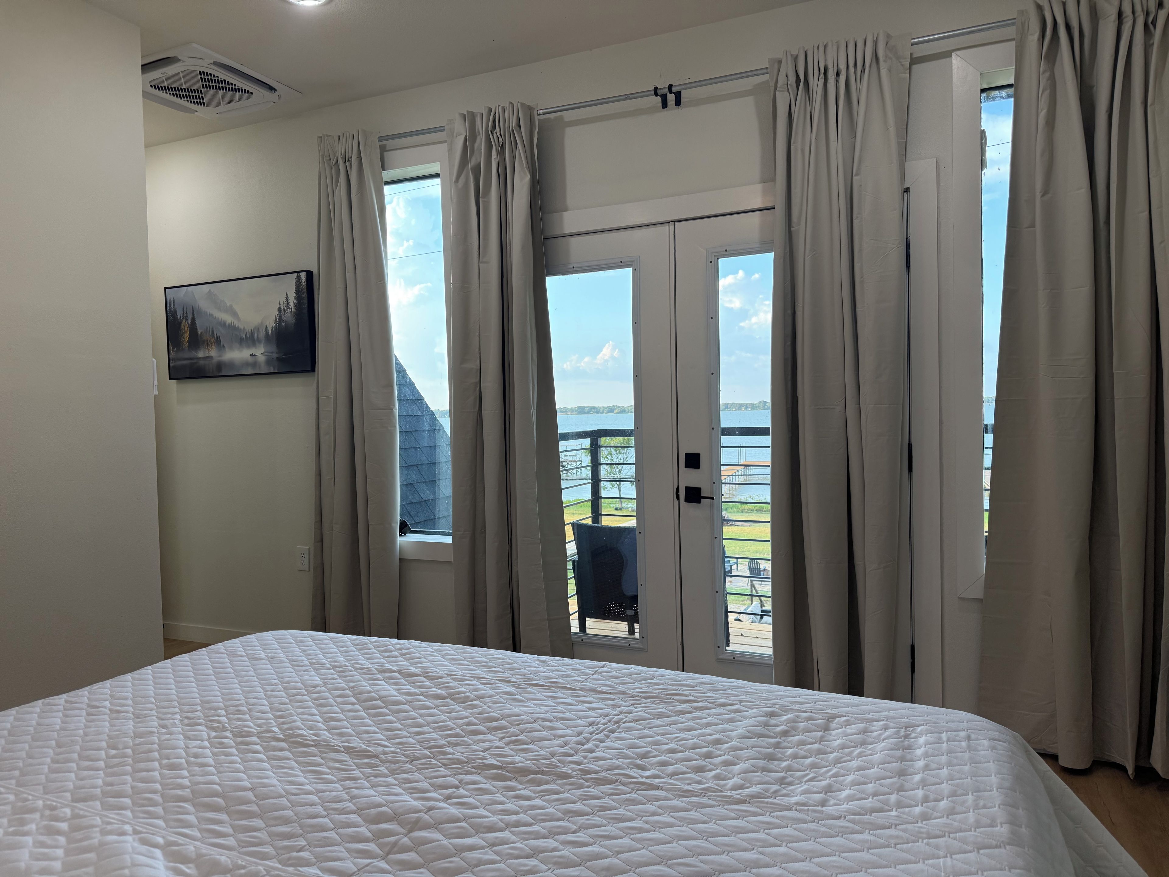 Ein Schlafzimmer mit einem großen Bett, einem Bild an der Wand und Blick auf einen Balkon mit einem Stuhl.