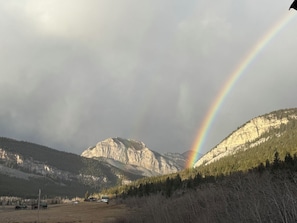 A mountain landscape with a rainbow, a clear sky, and a few buildings in the foreground. - Historic 5-bedroom log home in Choteau perfect for families or large groups (Choteau)