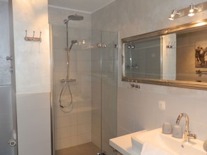 Ein modernes Badezimmer mit einer gläsernen Duschkabine, einem großen Spiegel und einem Waschbecken mit zwei Seifenspendern.