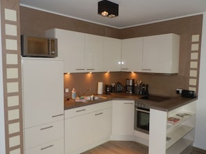A compact kitchen with white cabinets, a microwave, a coffee maker, and an oven. - "castle by the Sea" - Apt. 02 (Wyk auf Foehr)