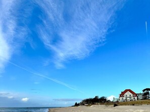 Een strand met een groot huis, heldere lucht en de oceaan.