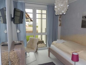 Ein Schlafzimmer mit einem Bett, einem Fernseher, einem Sessel und einem Fenster mit Vorhängen.