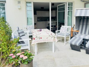 Eine Terrassengruppe mit Tisch und Stühlen, eine Glastür zum Küchenbereich und Kübelpflanzen.