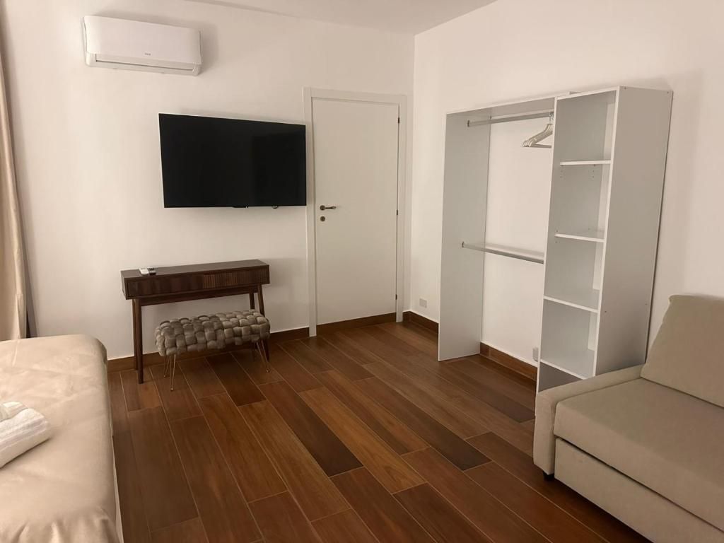 Una habitación con cama, televisor montado en la pared, piso de madera, un banco y un armario.
