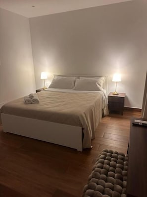 Un dormitori amb un llit, abacaments, un terra de fusta i una panxa.