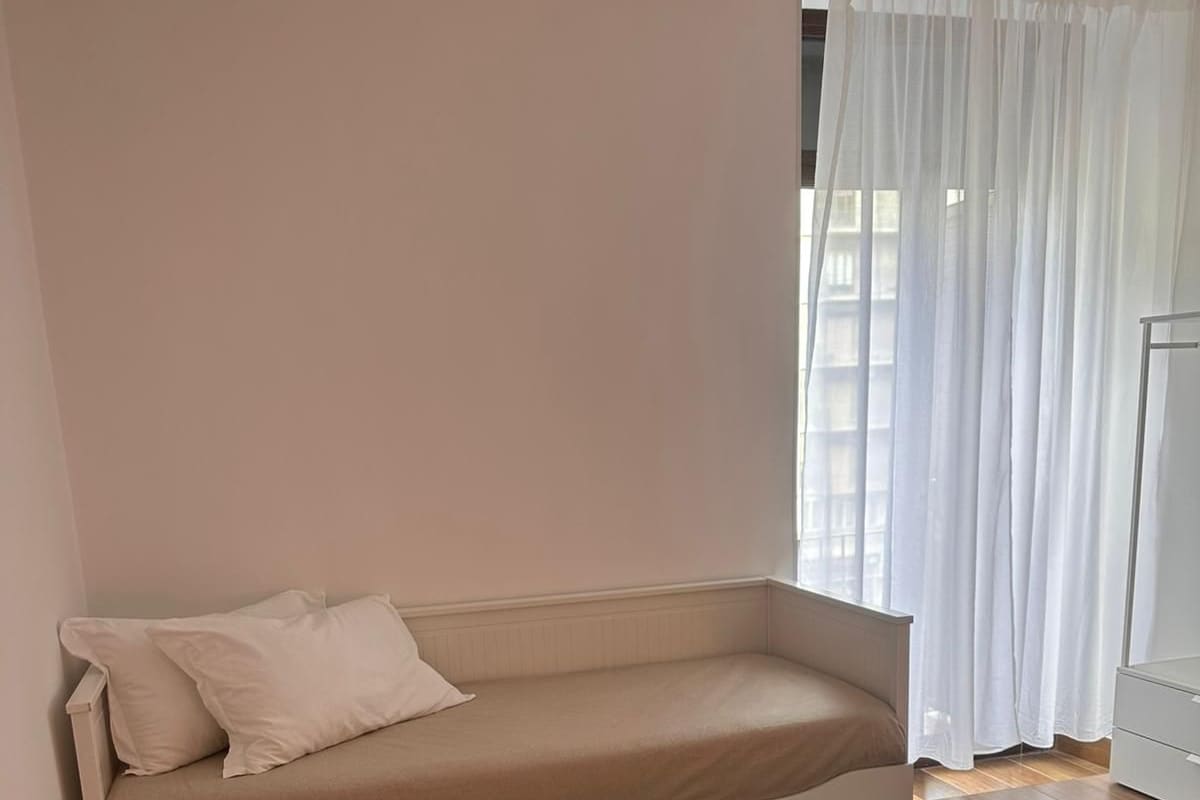 A bedroom with a bed, a sofa bed, a wardrobe, and a window with curtains.
