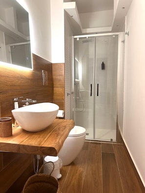 A modern bathroom with a large vessel sink, a toilet, and a glass-enclosed shower. - DAL CONSOLE (Catania)
