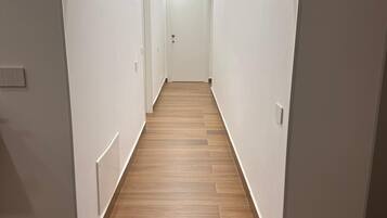 Un couloir étroit et bien éclairé, doté d’un plancher en bois et de murs blancs.