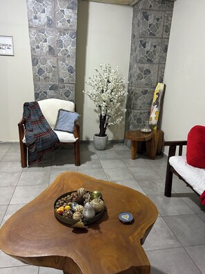 A living room with a stone wall, a wooden coffee table with decorative items, a chair with a blanket, and a painting on the wall. - Cozy 2-bedroom apartment in fantastic Santa Ana  El Salvador with AC (Santa Ana)