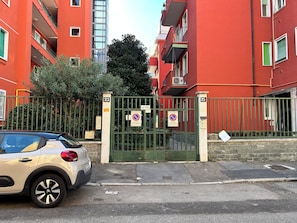 A gated residential area with red buildings, a car parked in front, and a no parking sign.