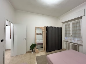 A bedroom with a bed, a door, a mirror, a window with blinds, and a radiator. - AntoBel House Milan – Private Apartment for 4 Guests Near the Metro (Milano)