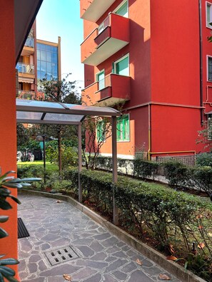 A courtyard with a covered seating area, stone flooring, and a red building with balconies. - AntoBel House Milan – Private Apartment for 4 Guests Near the Metro (Milano)