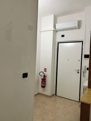 A hallway with a white door, a fire extinguisher mounted on the wall, and an air conditioning unit above the door. - AntoBel House Milan – Private Apartment for 4 Guests Near the Metro (Milano)
