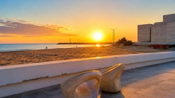 A sunset view from a balcony overlooking a beach with a stone sculpture in the foreground.
