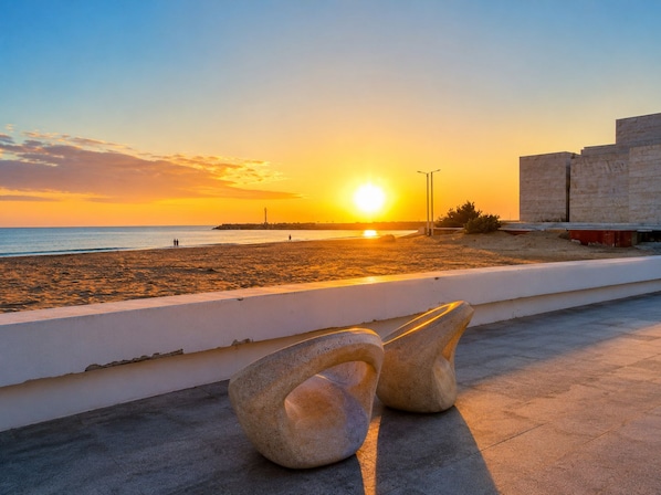 A sunset view from a balcony overlooking a beach with a stone sculpture in the foreground.