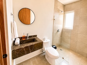A bathroom with a marble sink, a toilet, a shower, and a round mirror. - Vista al Mar a Pie de Playa 2 Tv Alberca (Playas del Conchal)
