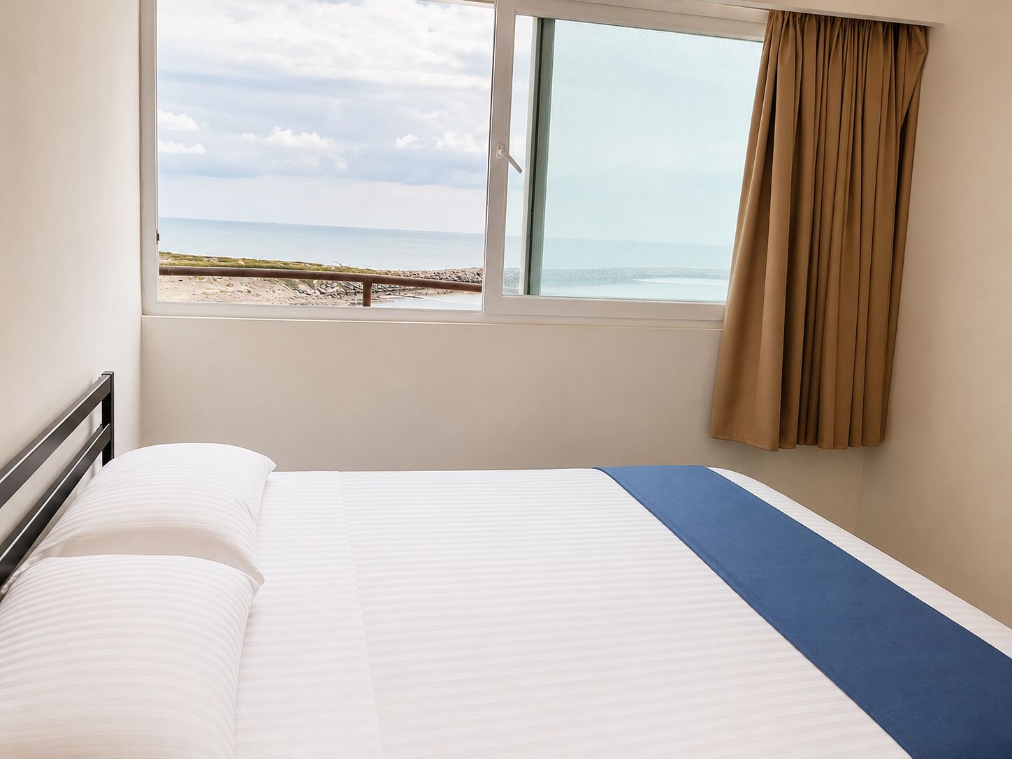 Una habitación de hotel con una cama, un ventanal con vistas a la playa y una cortina.