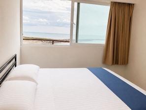 A hotel room with a bed, a window with a view of the beach, and a curtain.