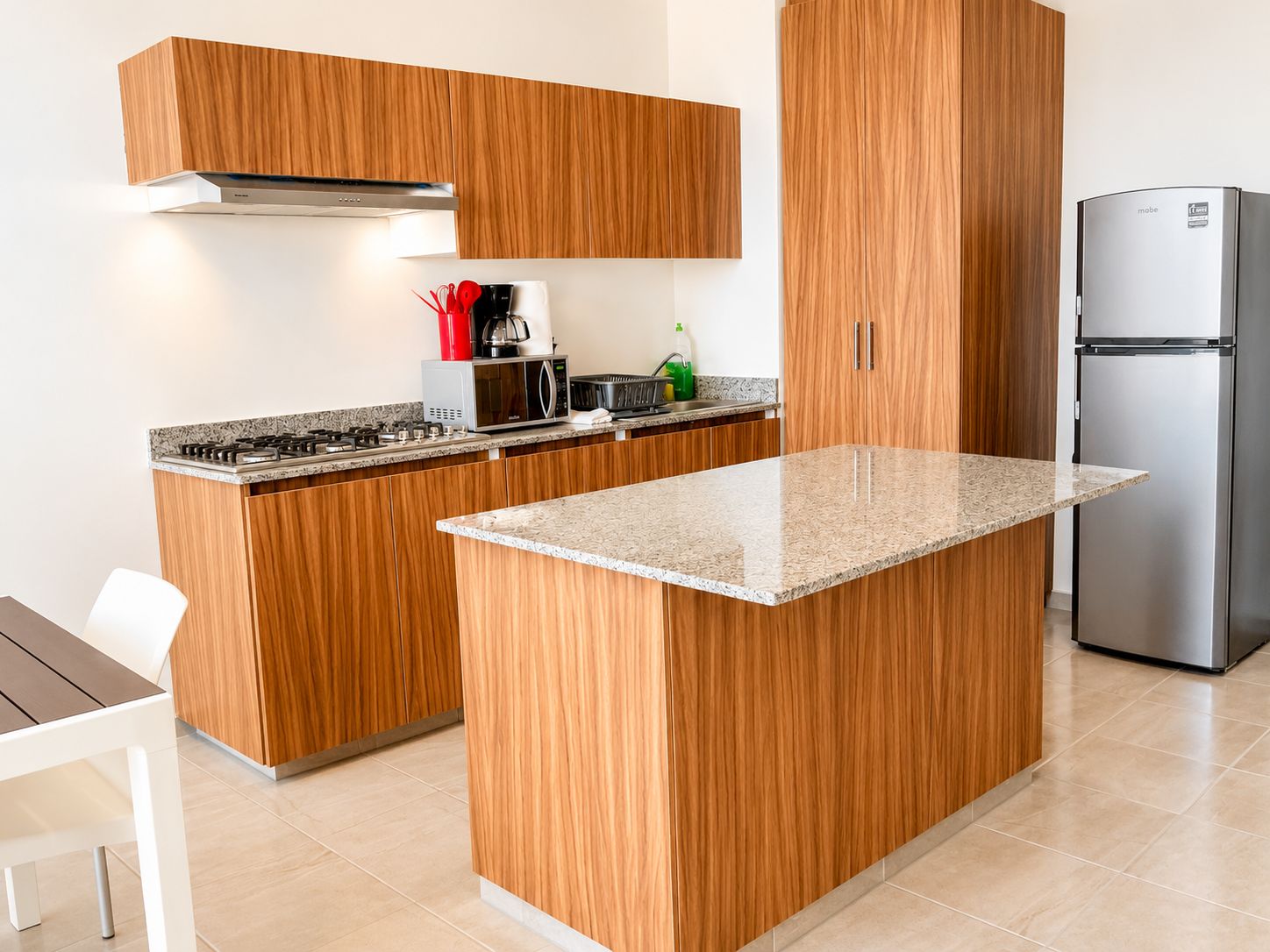 A modern kitchen with wooden cabinetry, a built-in island, stainless steel appliances, and a white dining area.