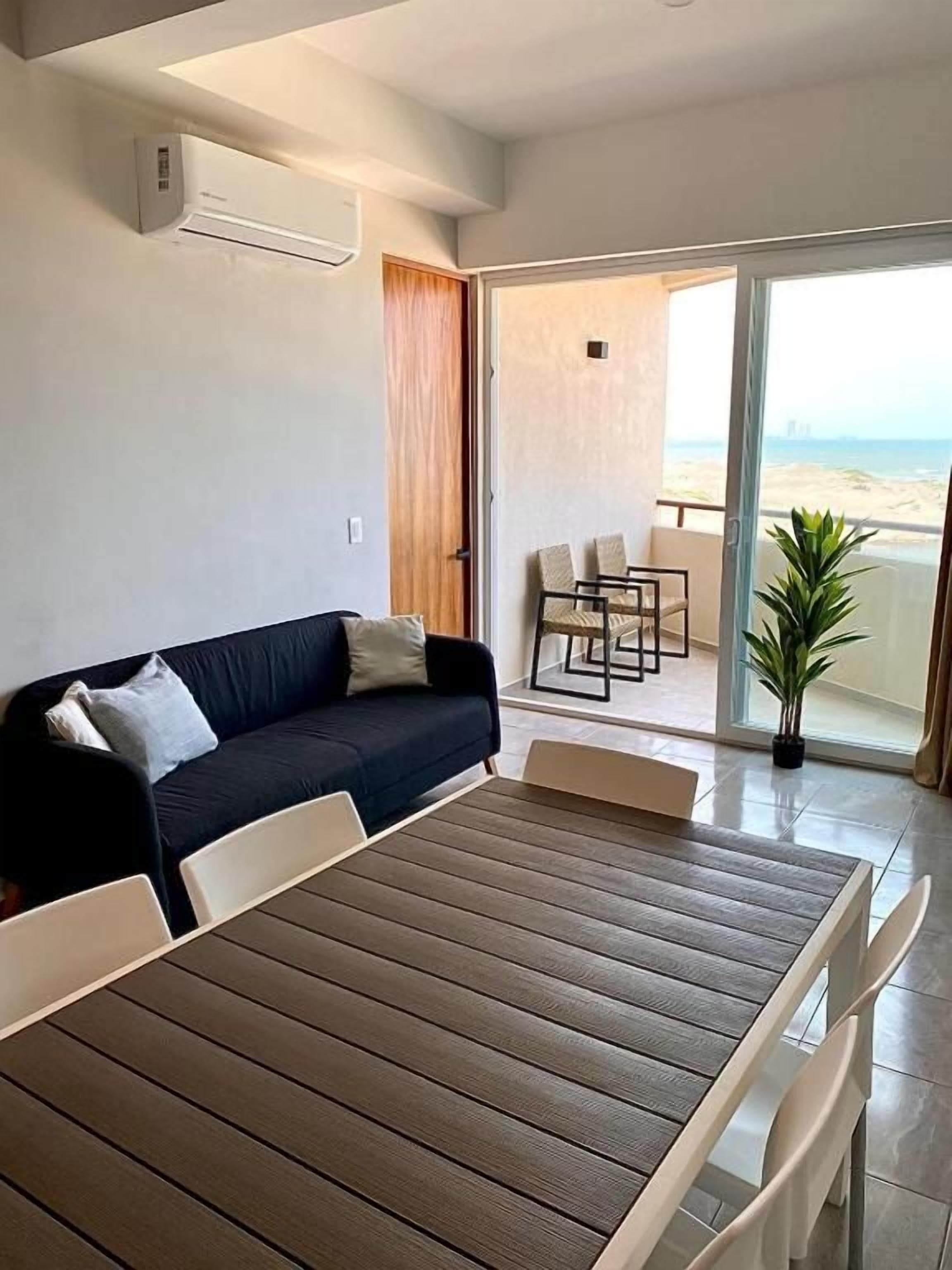 Habitació amb sofà, taula de menjador i vista a la platja a través d'una porta de vidre.