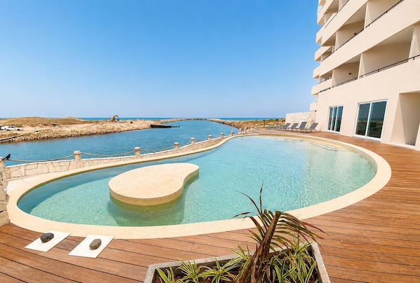 A swimming pool with a wooden deck, a stone wall, and a view of the sea. - Vista al Mar a Pie de Playa 2 Tv Alberca (Playas del Conchal)