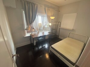 A small, compact room with a bed, a desk, a chair, and a window with curtains. - Steps to Main St Subway | 20 Min to Downtown (Toronto)