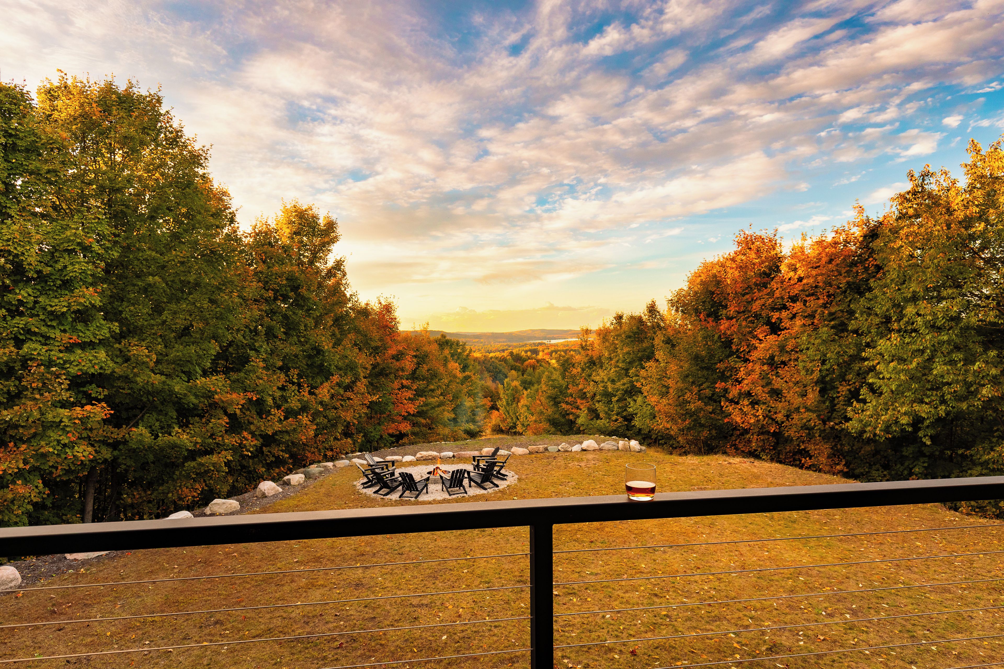 A scenic outdoor seating area with a fire pit, surrounded by trees and a view of the landscape.