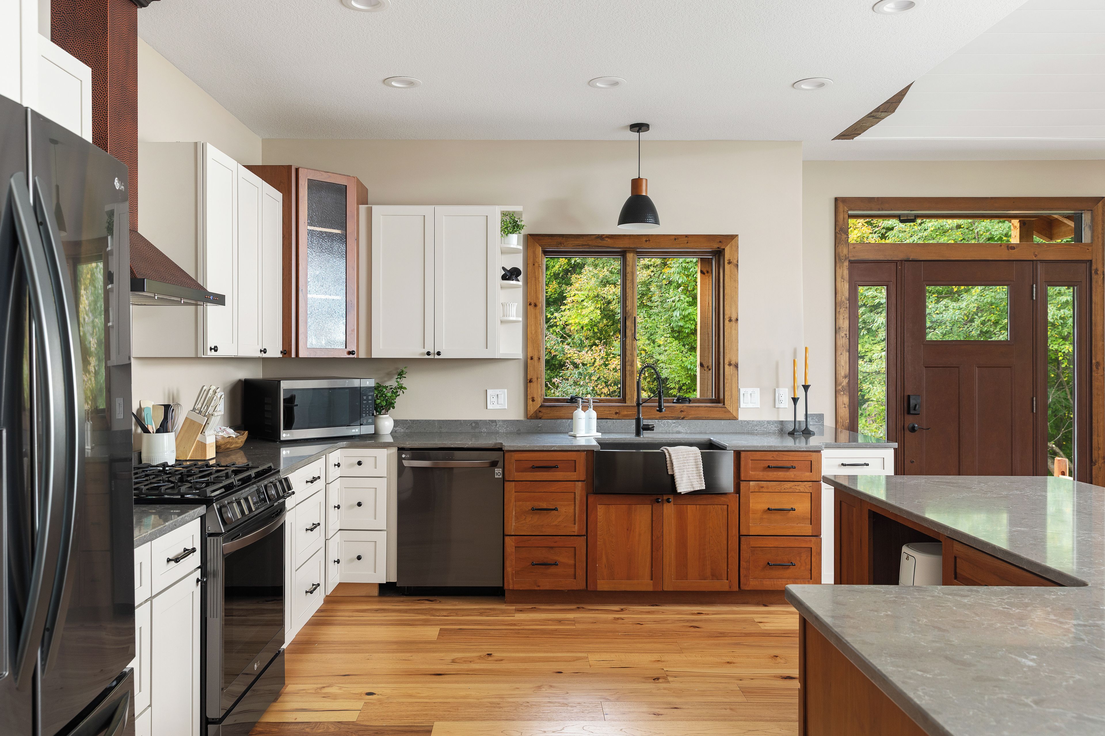 A modern kitchen with stainless steel appliances, wooden cabinets, and a large window providing a view of greenery.