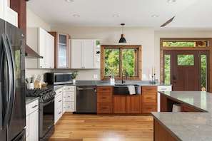 A modern kitchen with stainless steel appliances, wooden cabinets, and a large window providing a view of greenery. - Long-Range Lake Views | Sauna, Plunge, Hot Tub (Bellaire)