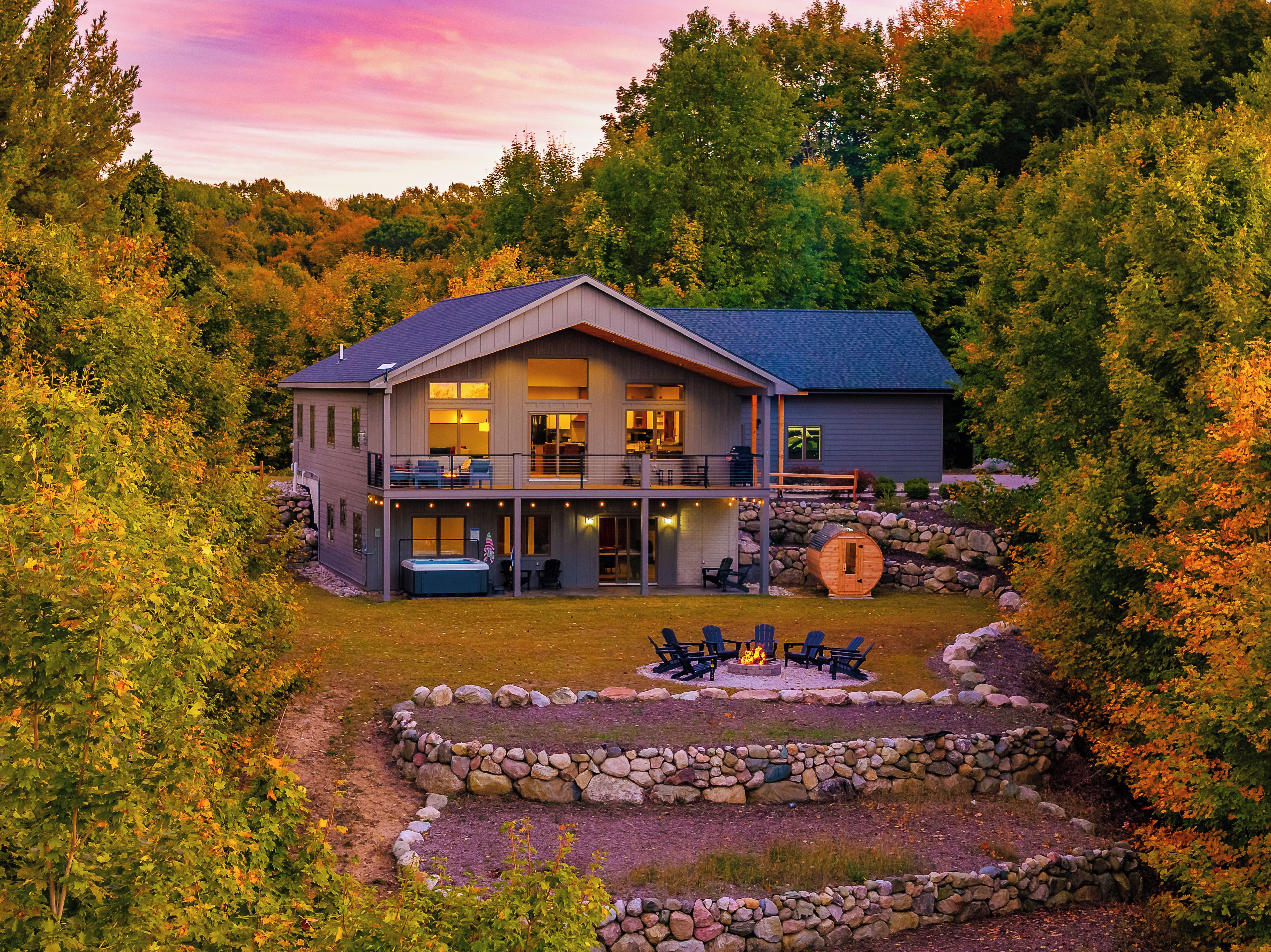 A two-story house with a balcony, a hot tub, and a stone fire pit surrounded by a stone wall.