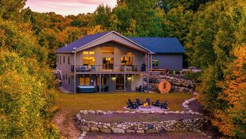 A two-story house with a balcony, a hot tub, and a stone fire pit surrounded by a stone wall.