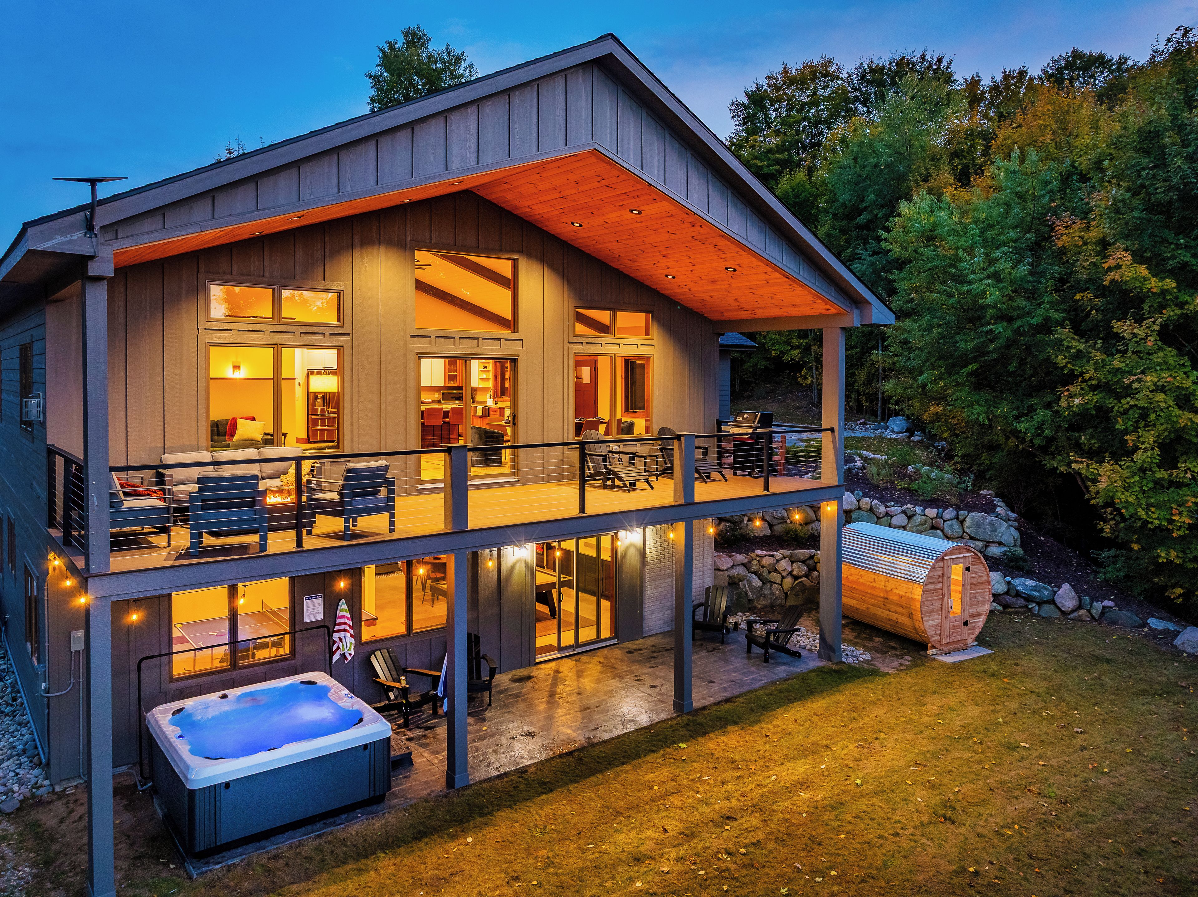 A two-story house with a balcony, a hot tub, and a stone wall.