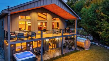 A two-story house with a balcony, a hot tub, and a stone wall.