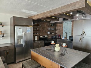 A modern kitchen with a central island, stainless steel appliances, and a herringbone-patterned backsplash. - Rising Tides Properties Condo 204 (Murrells Inlet)