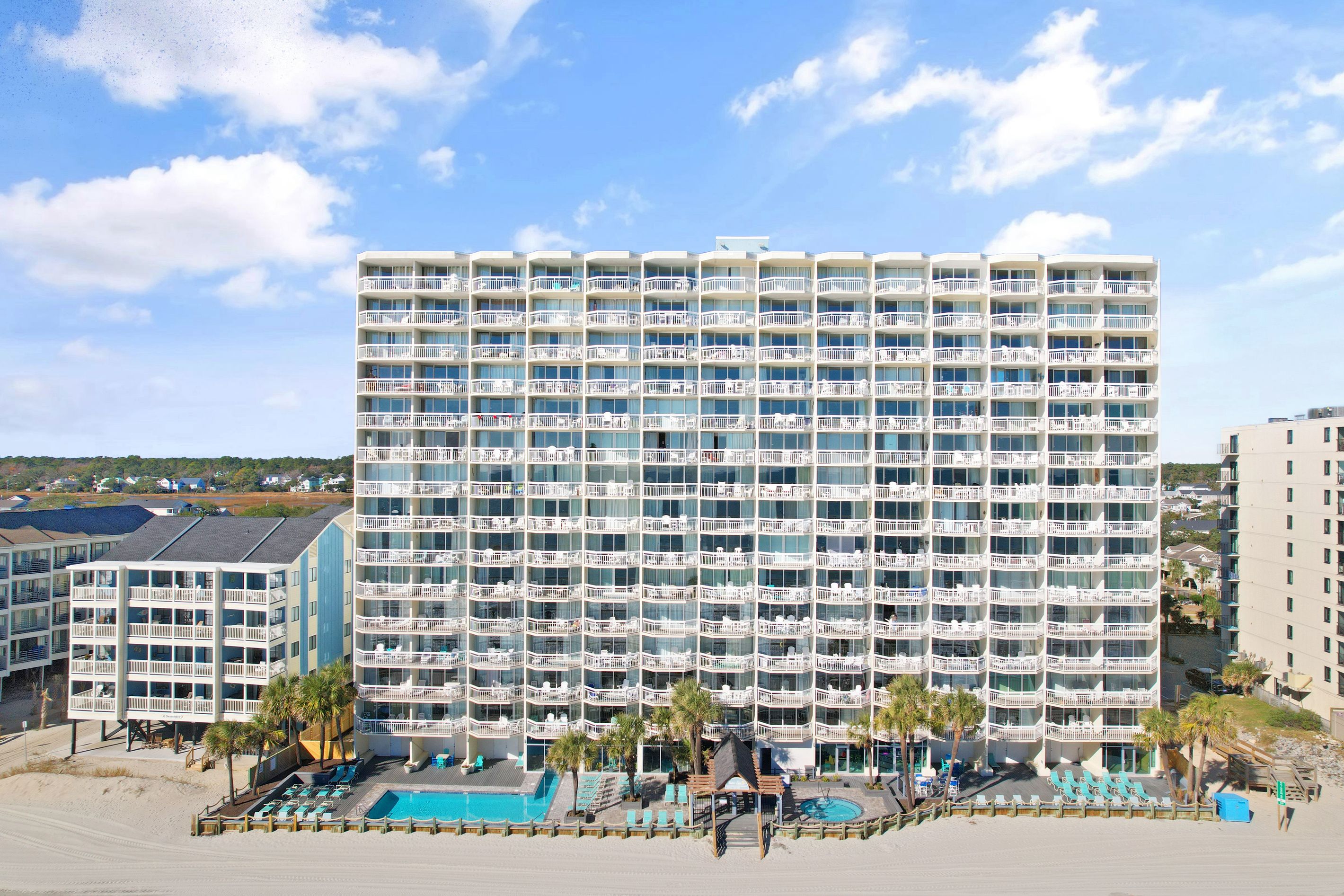 A multi-story hotel with balconies, a pool area, and a beach view.