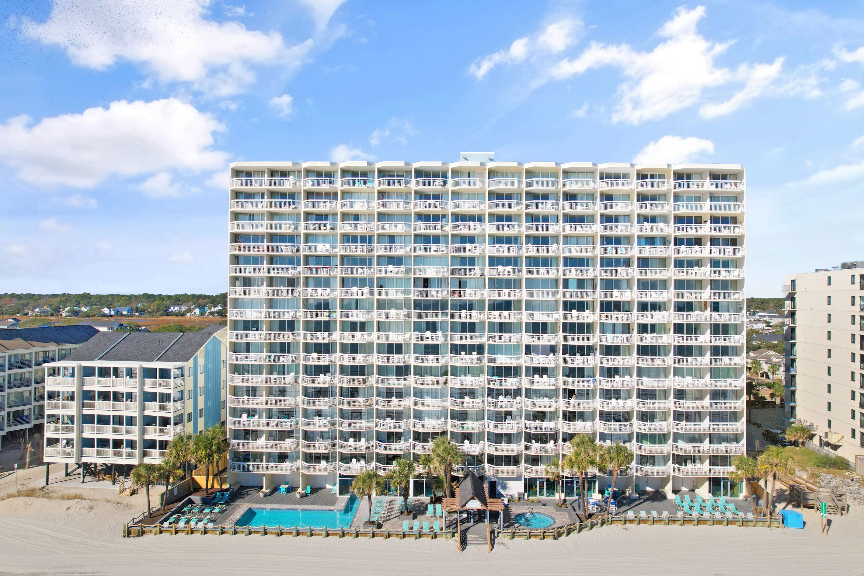 A multi-story hotel with balconies, a pool area, and a beach view.