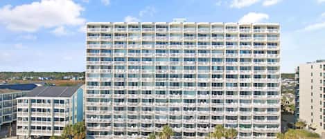 A multi-story hotel with balconies, a pool area, and a beach view.
